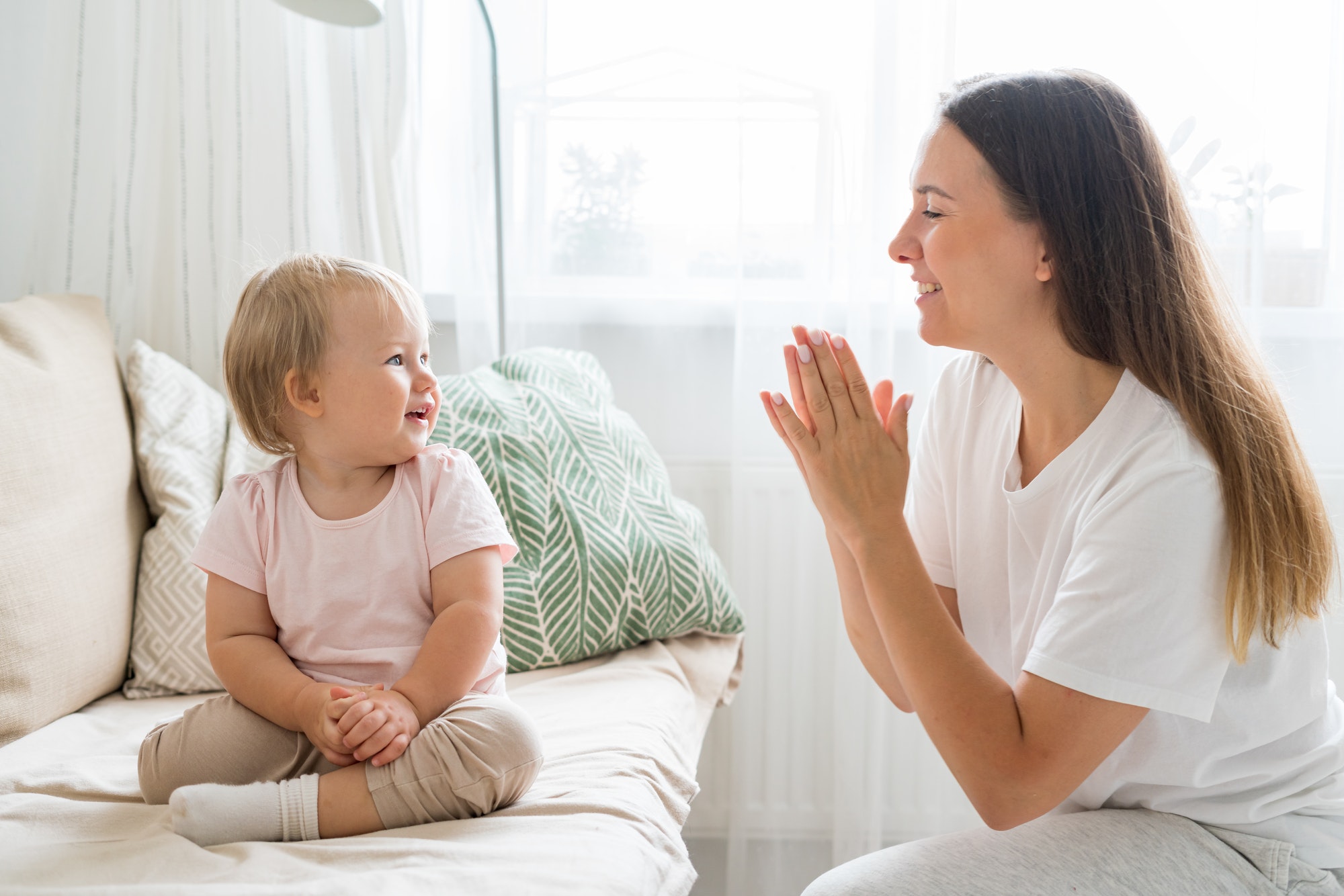 smiling-mother-clapping-and-looking-at-happy-toddler-sitting-on-couch-in-living-room.jpg