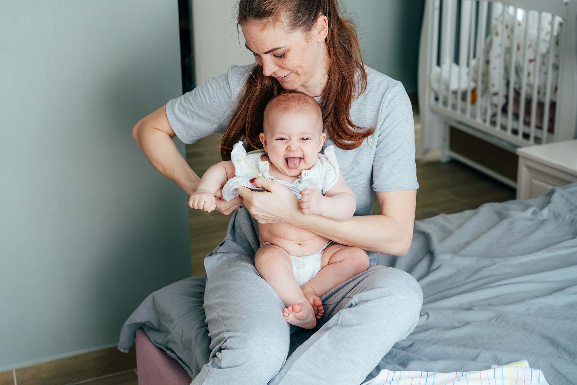 a-young-mother-is-dressing-up-her-cheerful-infant-VBYJ6VX.jpg